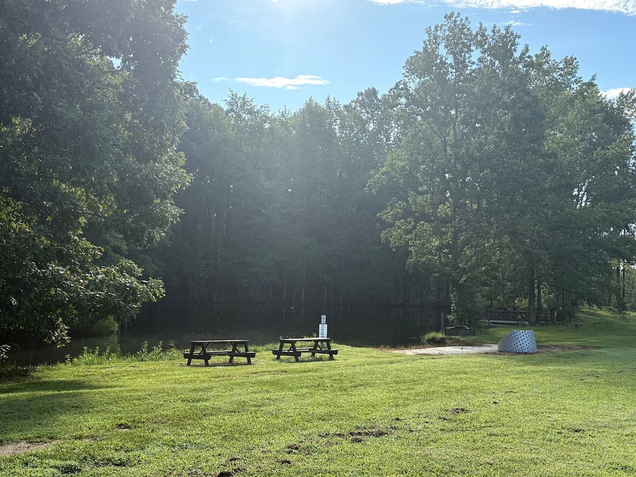 A picnic area with two picnic tables and a sign, surrounded by trees and grass.