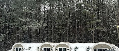 A row of dome-shaped cabins with arched doorways, surrounded by a wooden fence and a snowy landscape.
