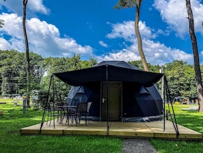 A tent with a table and chairs set up on a grassy area with trees in the background.