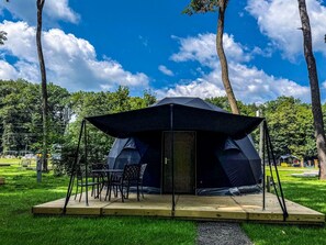 Una carpa con una mesa y sillas dispuestas en un área cubierta de césped, con árboles al fondo.