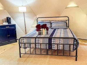 Una cama individual con estructura metálica, colchón acolchado y una lámpara de noche.