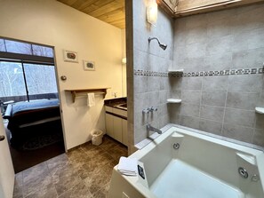 Un baño con bañera, ducha y lavamanos. Se ve una ventana con vistas a árboles.