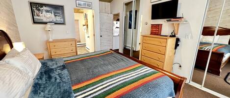 Une chambre à coucher avec un lit, une commode, un miroir et un téléviseur.