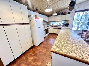 A kitchen with white cabinets, a patterned countertop, and a view of trees through a window.
