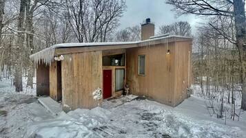 A wooden cabin with a red door, a chimney, and a snow-covered ground.