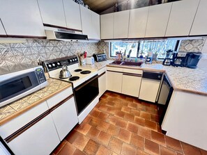 Cuina amb armaris blancs, microones, fogó, torradora i rentavaixelles.