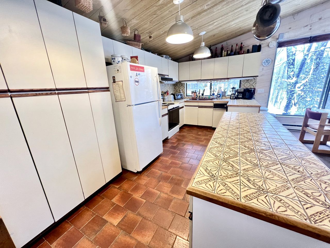 A kitchen with white cabinets, a patterned countertop, and a view of trees through a window.