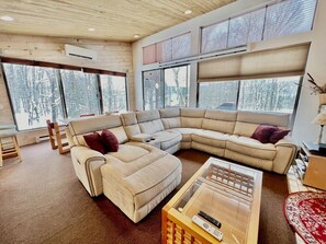 Una sala de estar moderna con un sofá modular, una mesa de centro de vidrio y ventanas amplias que dan a un paisaje nevado.