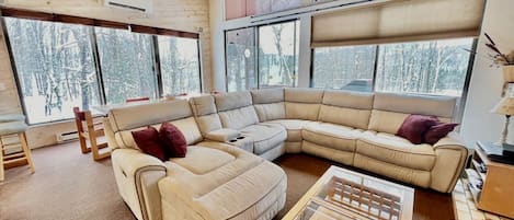 A modern living room with a sectional sofa, a glass coffee table, and large windows offering a view of a snowy landscape.