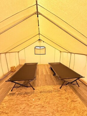 Una carpa con dos camas plegables, una lámpara colgante y suelo de madera.