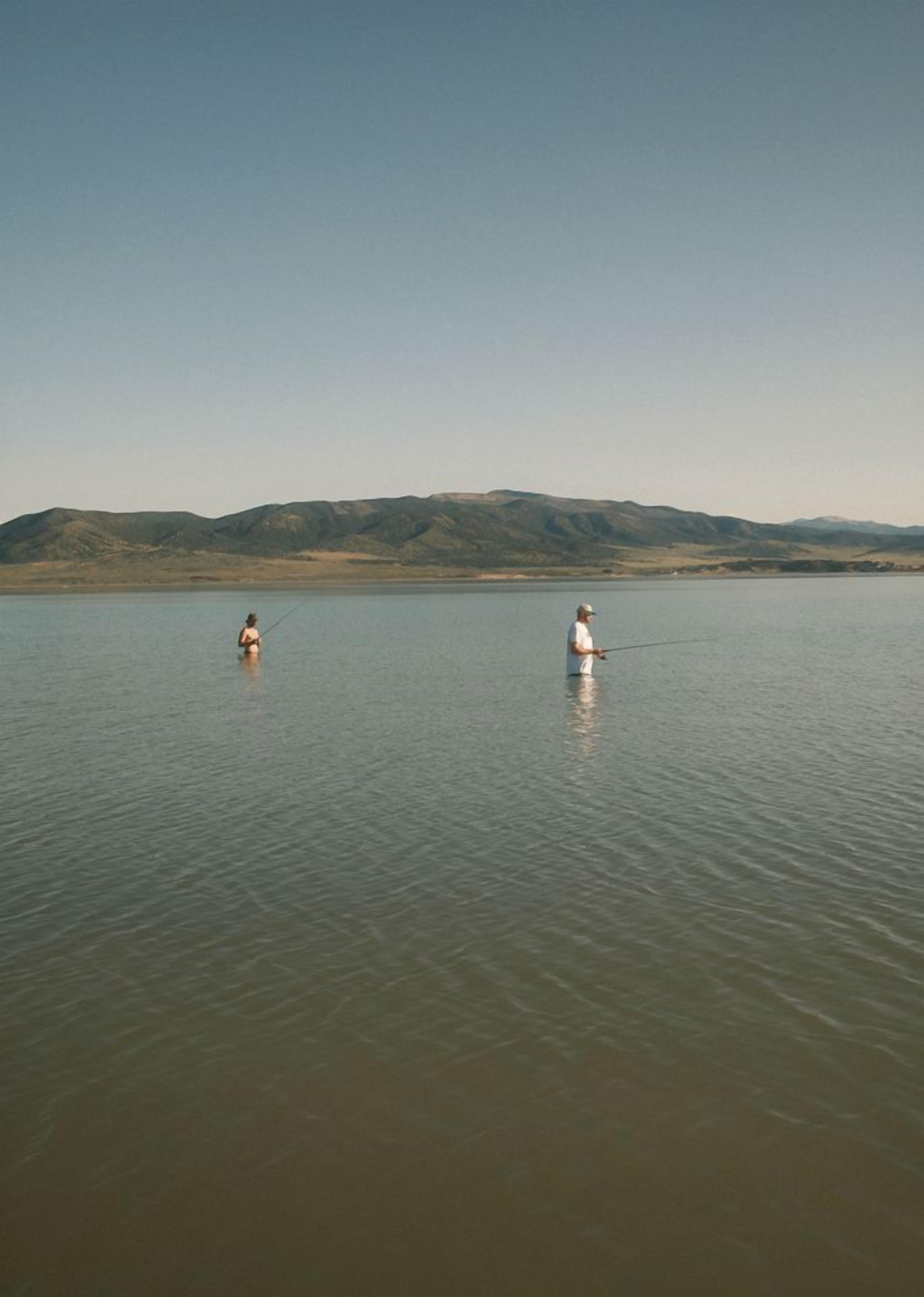 Um lago tranquilo com duas pessoas pescando, cercado por montanhas.