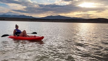 Una persona practica kayak en aguas tranquilas, con montañas al fondo.