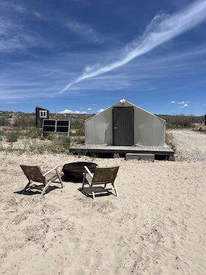 A beach with two wooden chairs, a small shed, and a larger building with a door. - Spacious Pet-Friendly Safari Tent on Yuba Lake with Spectacular Views for a Memorable Glamping Escape in Utah (Levan)