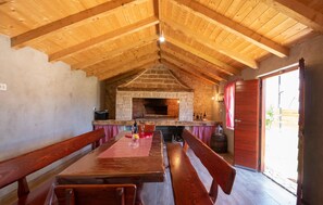 Ein rustikales Interieur mit Kamin aus Stein, Holzbalken und einem Essbereich mit Bänken.