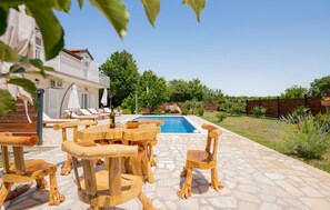 Ein Poolbereich mit Holzmöbeln, einem klaren, blauen Pool und einem Haus im Hintergrund.