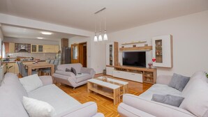 Un salon moderne avec un ensemble de canapés, une table basse, un téléviseur et une cuisine en arrière-plan.
