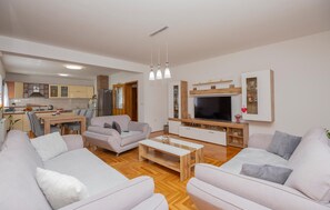 Ein modernes Wohnzimmer mit einer Sofagarnitur, einem Couchtisch, einem Fernseher und einer Küche im Hintergrund.