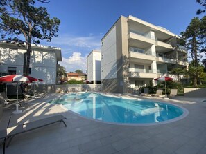 Ein modernes Gebäude mit Schwimmbad, Liegestühlen und Sonnenschirmen.