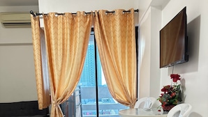 Une chambre d’hôtel comprenant un lit, une table à manger avec des chaises, un téléviseur fixé au mur et une vue sur la ville grâce à de grandes fenêtres.