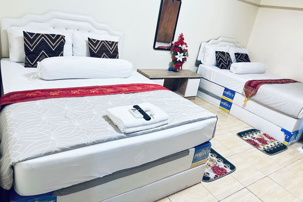 A hotel room with two beds, a small table, a mirror, and a floral decoration.