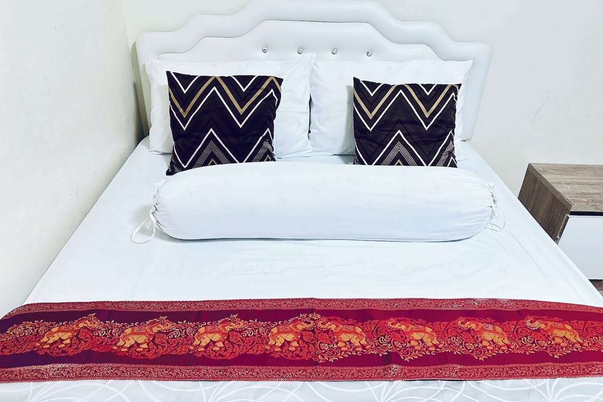 A bed with a white headboard, two patterned pillows, a white pillow, and a red decorative border.