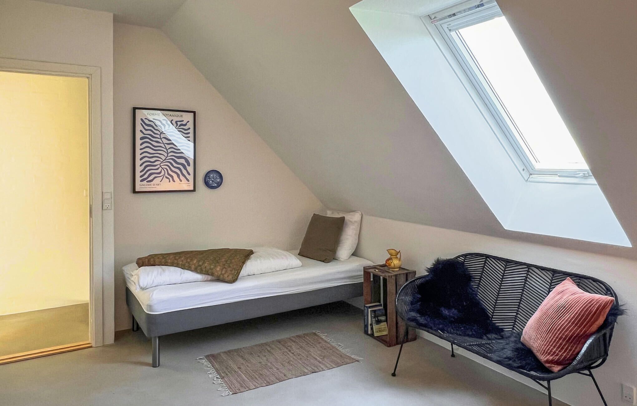 Une chambre de style loft avec un plafond en pente, un lit, une chaise, une petite table et un puits de lumière.