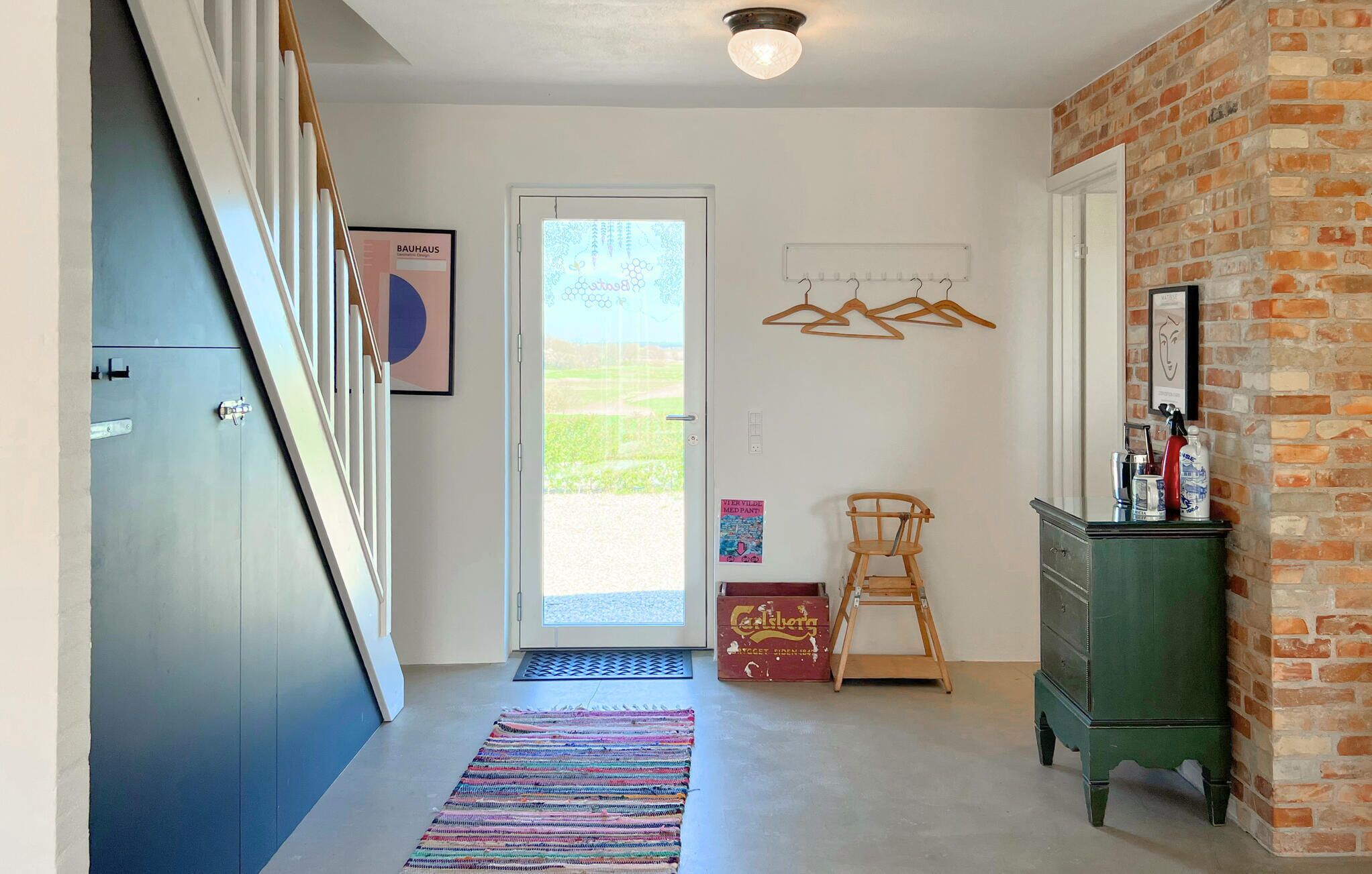 A hallway with a door leading outside, a wooden chair, a green dresser, and a hanging rack with clothes.