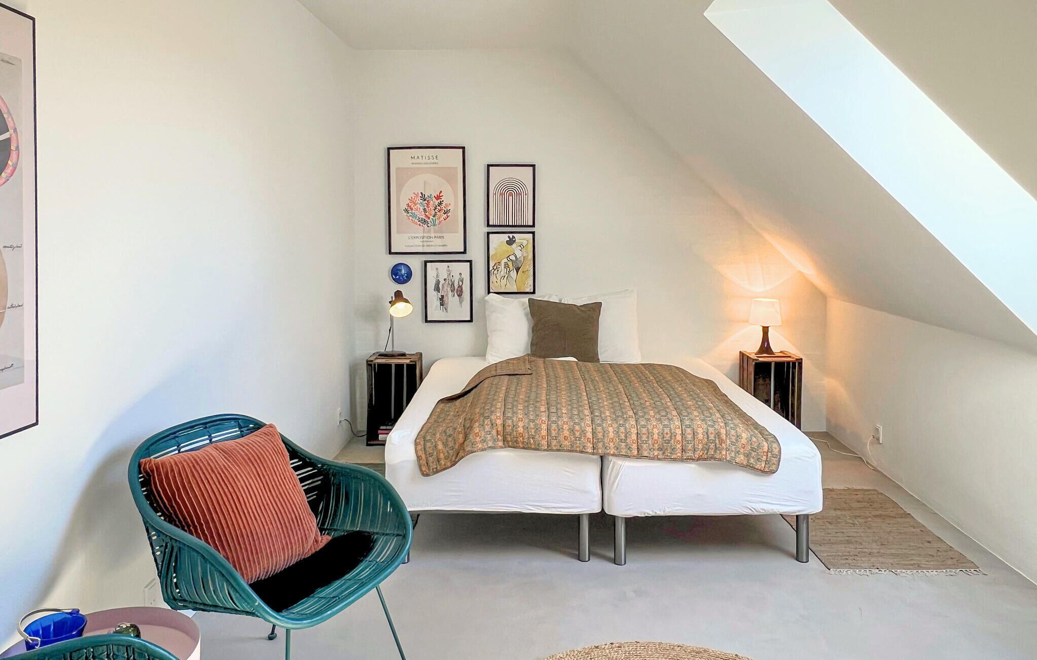 Ein Schlafzimmer mit einem Bett, zwei Nachttischen, einem Sessel und Wandbildern.