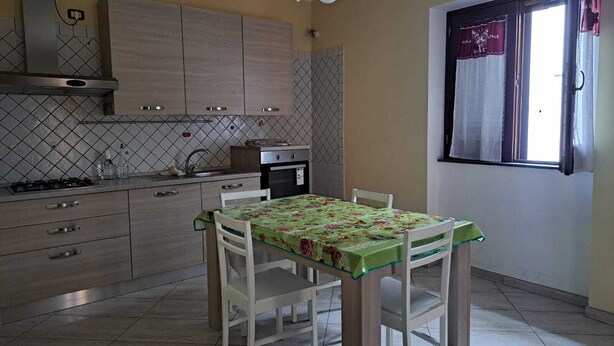 A kitchen with a dining table, cabinets, and a window with curtains. - Cirillo House Marigliano (Marigliano)