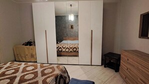 A bedroom with a wardrobe, a bed with patterned bedding, a small table with a cloth, and a dresser. - Cirillo House Marigliano (Marigliano)