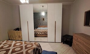 Una camera da letto con un armadio, un letto con copriletto decorato, un tavolino con una tovaglia e un comò.