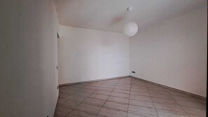 Una stanza con pavimento piastrellato, pareti bianche e una singola lampada a sospensione bianca.