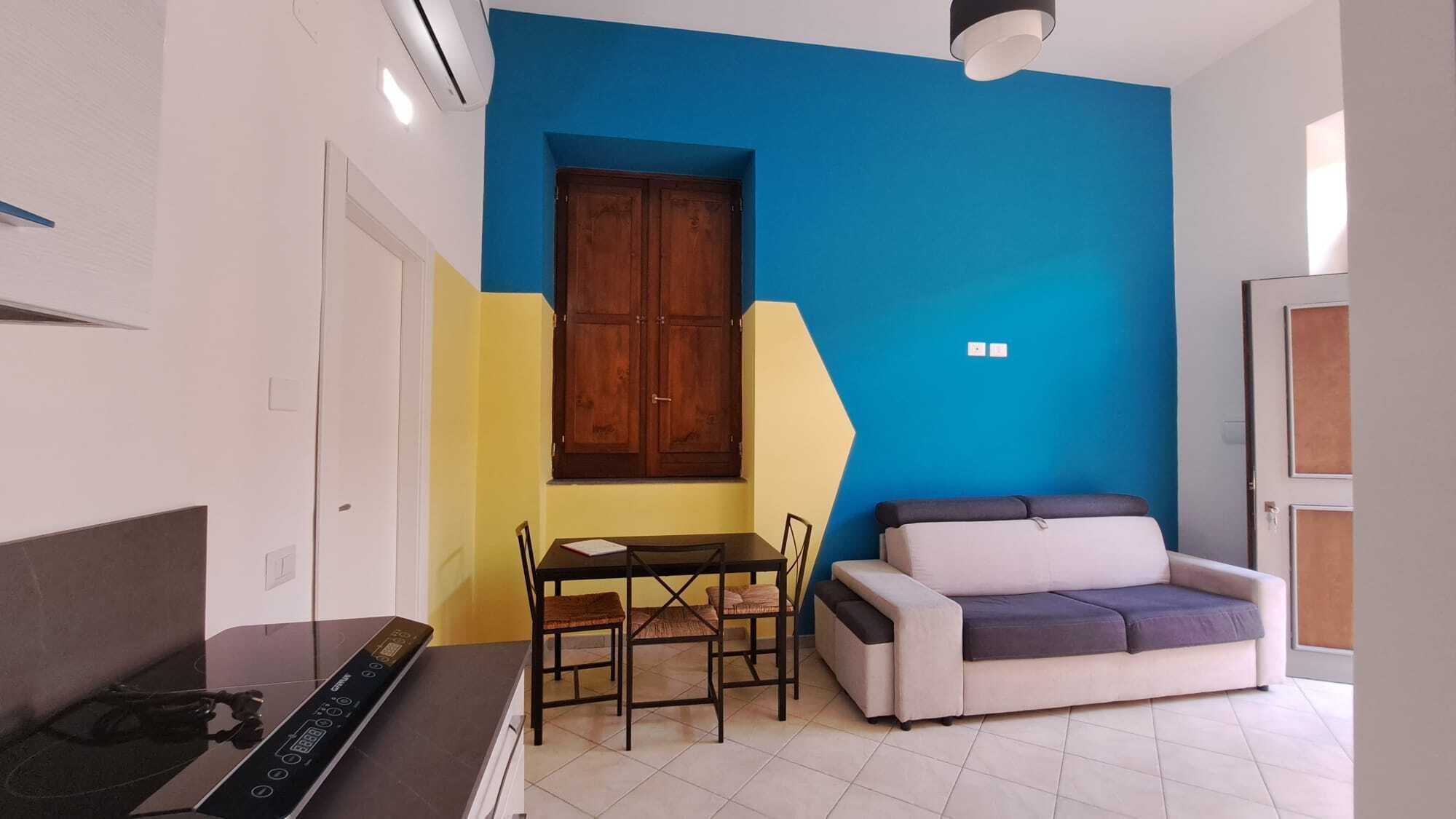 Un petit salon avec un canapé, une table à manger et des chaises, un téléviseur et une fenêtre avec une porte en bois.