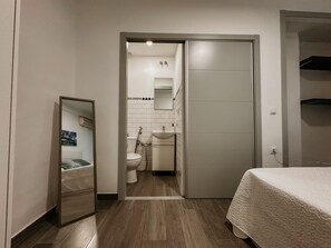 Une chambre à coucher comprenant un lit, un miroir, une armoire et une salle de bain avec des toilettes et un lavabo.