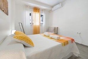 Une chambre d’hôtel avec un lit, une chaise, une fenêtre avec des rideaux et un appareil de climatisation.