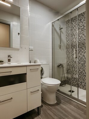Un baño moderno con inodoro, cabina de ducha y tocador con cajones y espejo.