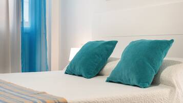 Un lit recouvert d’une couverture blanche à texture, agrémenté de deux coussins turquoise et d’une couverture à carreaux.
