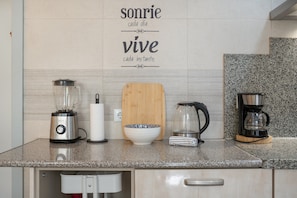 Un plan de travail de cuisine avec un mixeur, un saladier, une planche à découper, une bouilloire et une machine à café.
