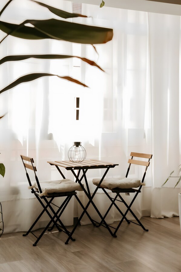 Une pièce avec une table et deux chaises, une plante et des rideaux légers.