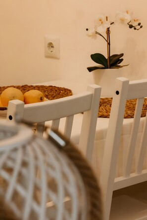 Una silla blanca con una cesta tejida en el respaldo, una planta de orquídea blanca y limones sobre un tapete tejido.
