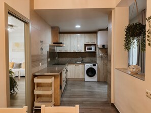 Cocina compacta con lavadora, microondas y una planta colgante.