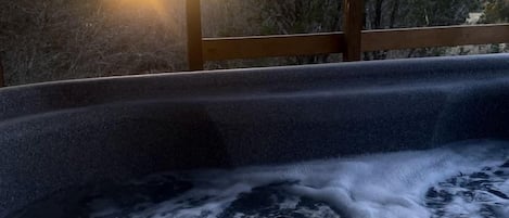 A hot tub with a wooden deck and a view of trees and the sky.