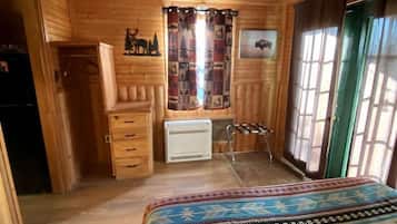 Habitación de cabaña de madera con cama, ventilador de techo, radiador y ventana con cortinas.