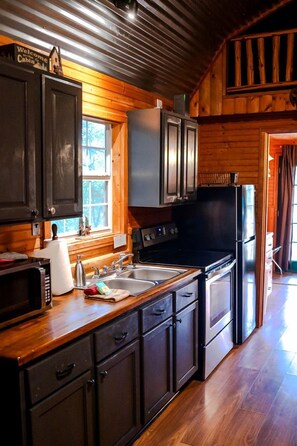 Una cocina tipo cabaña con paredes de madera, una ventana y un refrigerador.