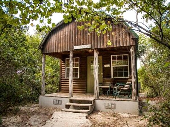 A rustic wooden cabin with a porch, a signboard, and a bicycle.