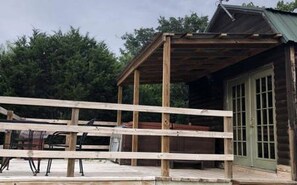 A wooden structure with a roof, possibly a porch or deck, adjacent to a building with a green door. - Vacation Cabin Rental with a Private Hot Tub near Fort Worth, Texas (Bluff Dale)