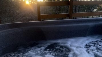 Un jacuzzi con terraza de madera y vistas a árboles y al cielo.