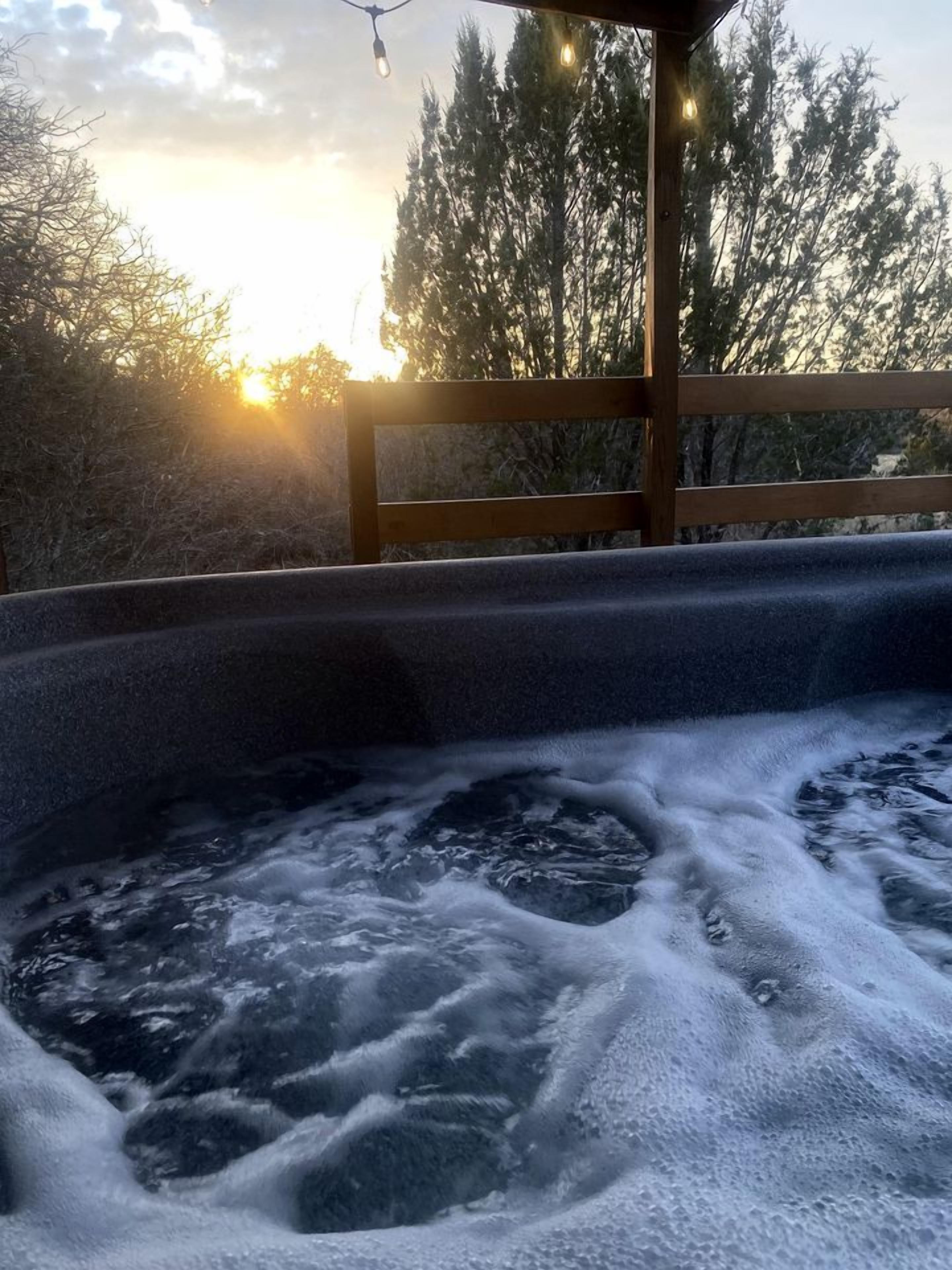 A hot tub with a wooden deck and a view of trees and the sky.