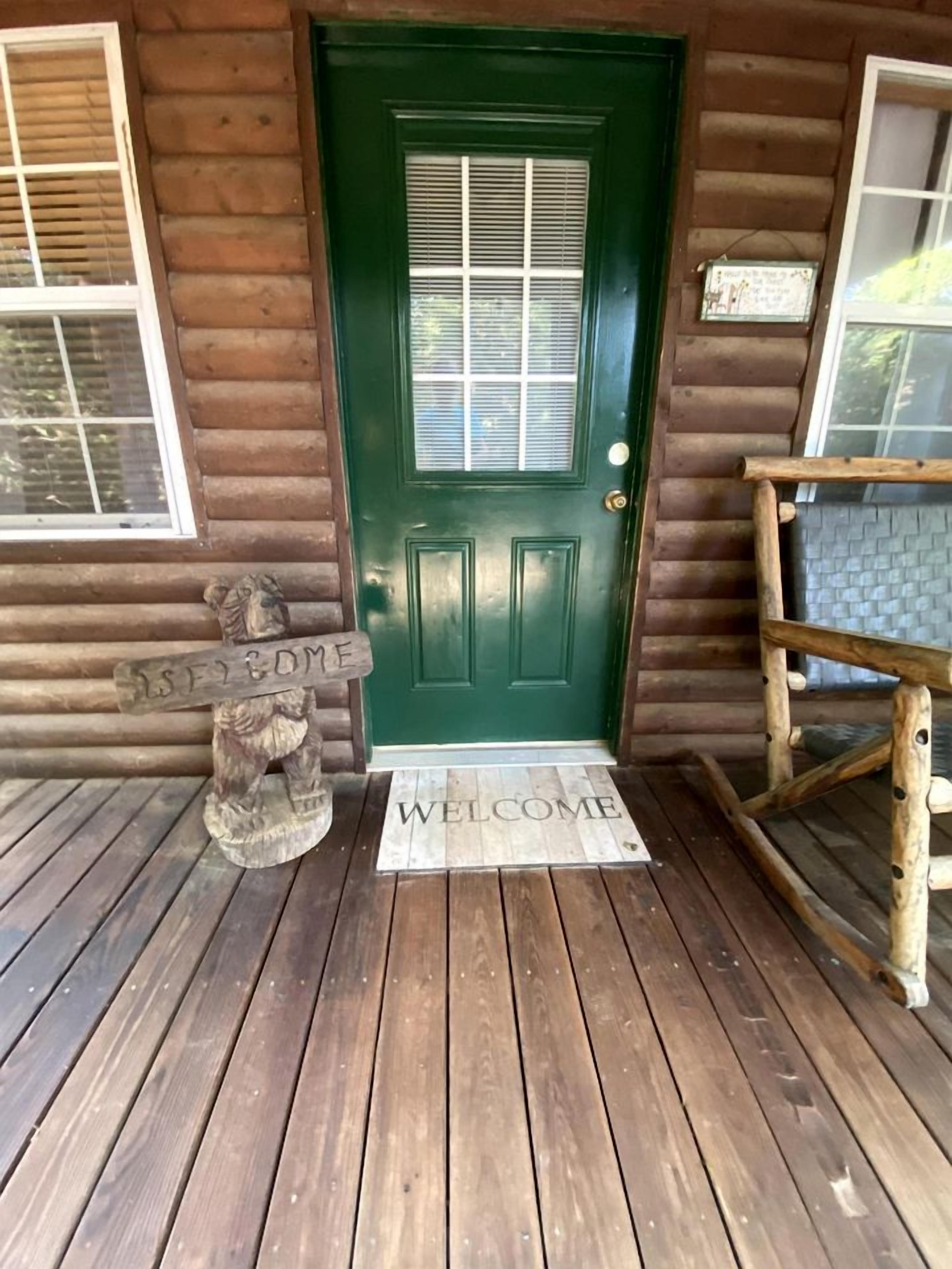 A wooden cabin with a green door, a welcome mat, and a wooden bench.
