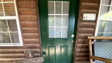 A wooden cabin with a green door, a welcome mat, and a wooden bench.